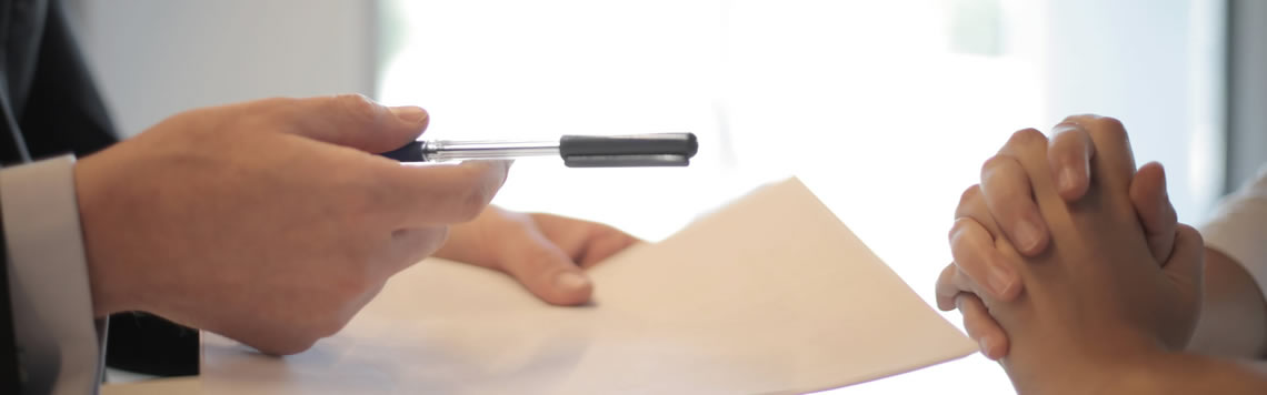 A picture of someone offering a pen and paper for someone else to sign.